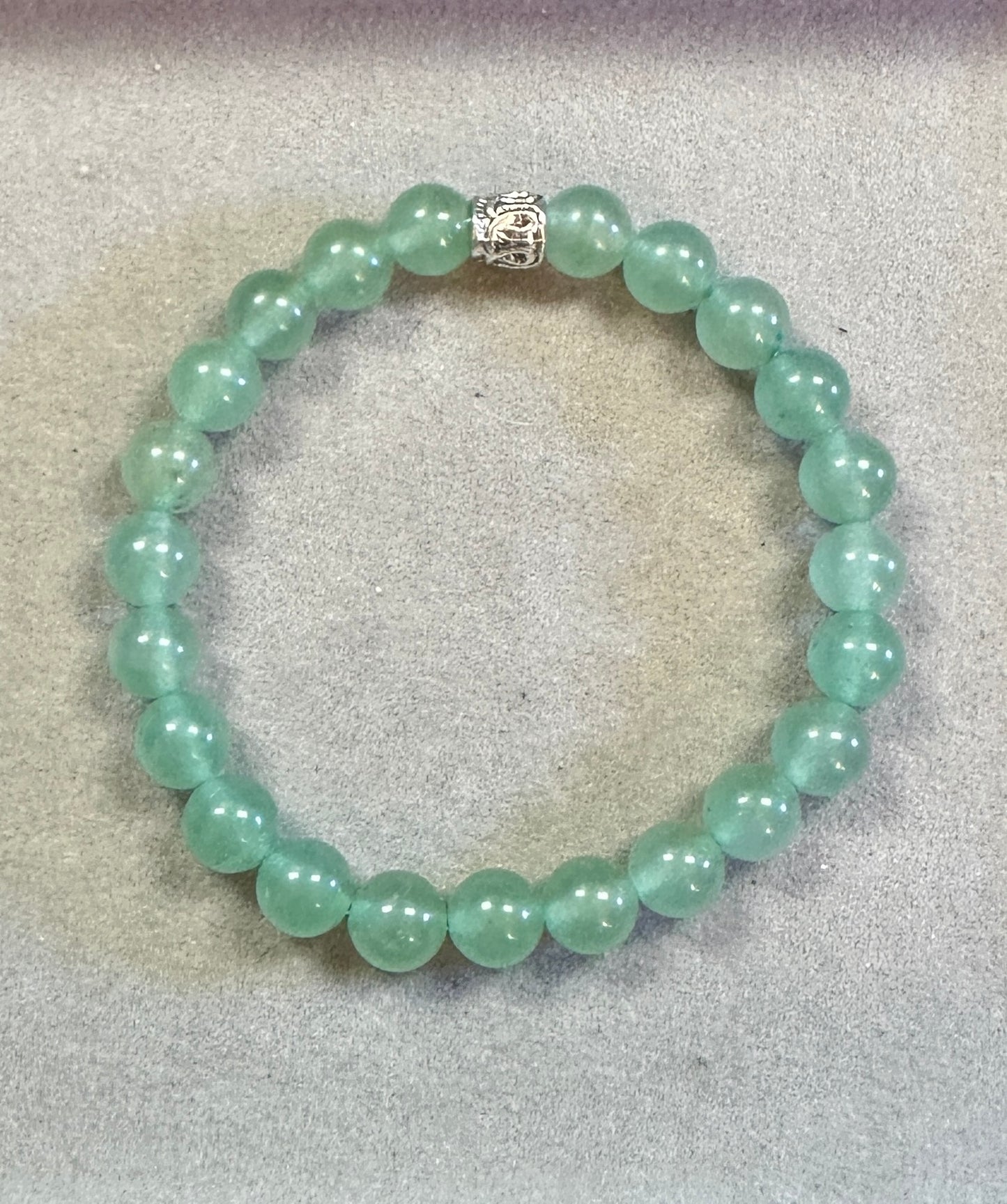 Green beaded bracelet with a silver clasp on a gray background