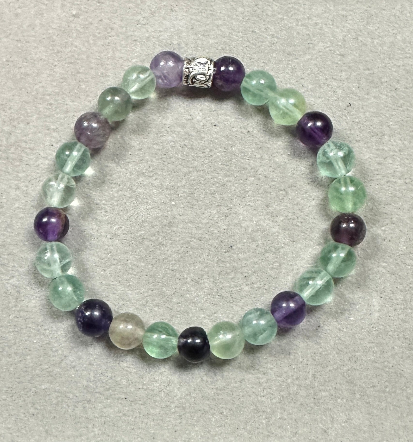 Beaded bracelet with green, purple, and clear beads on a gray background
