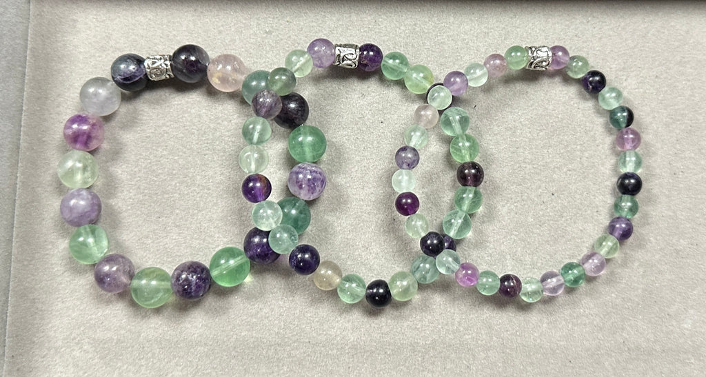 Set of three beaded bracelets with purple, green, and black beads on a light gray background