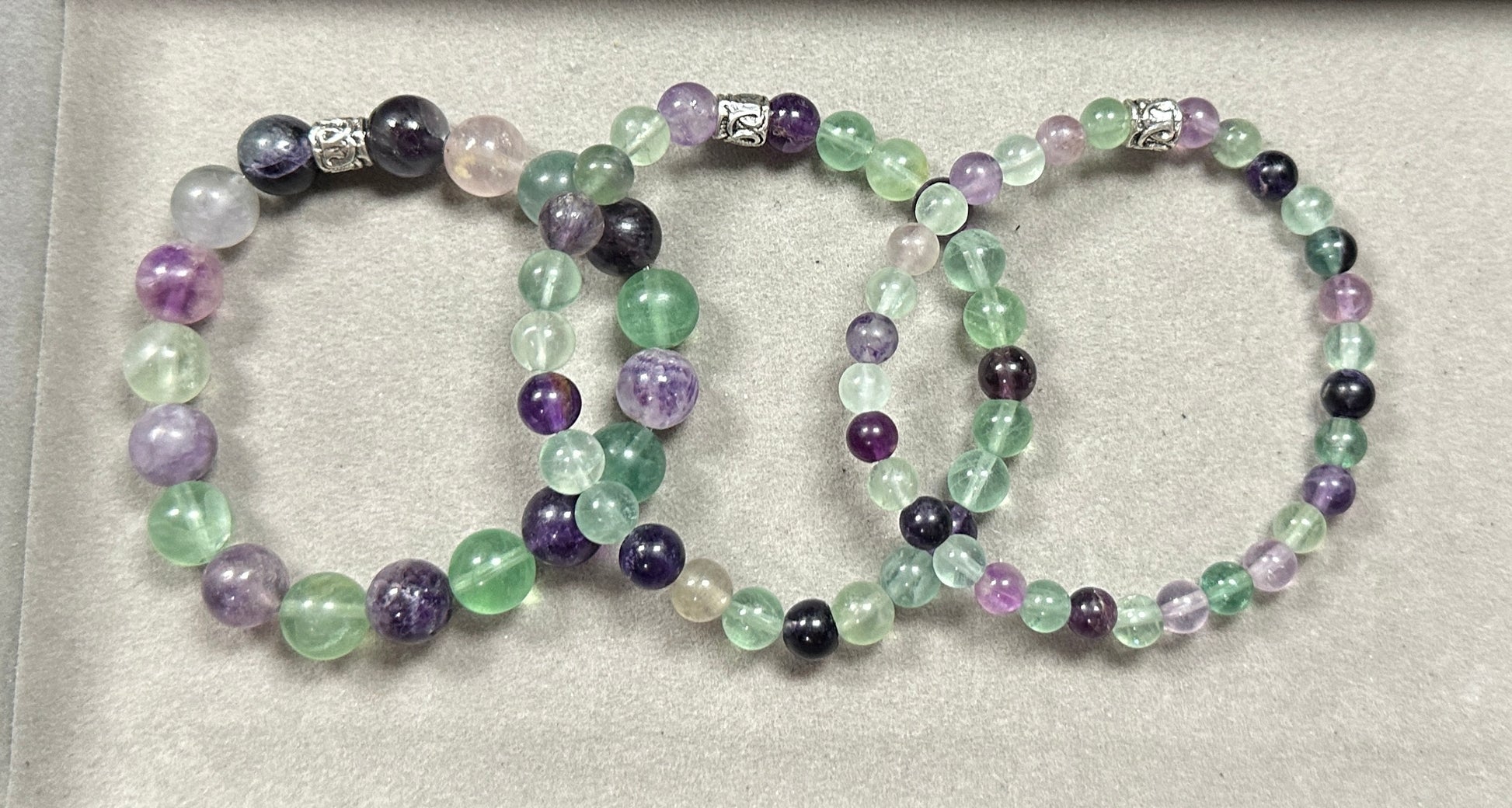Set of three beaded bracelets with purple, green, and black beads on a light gray background