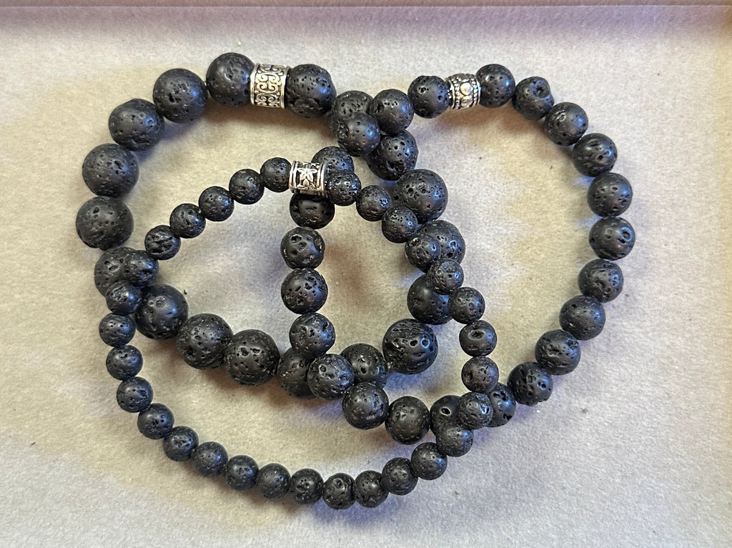 Set of black beaded bracelets with silver charms on a light background