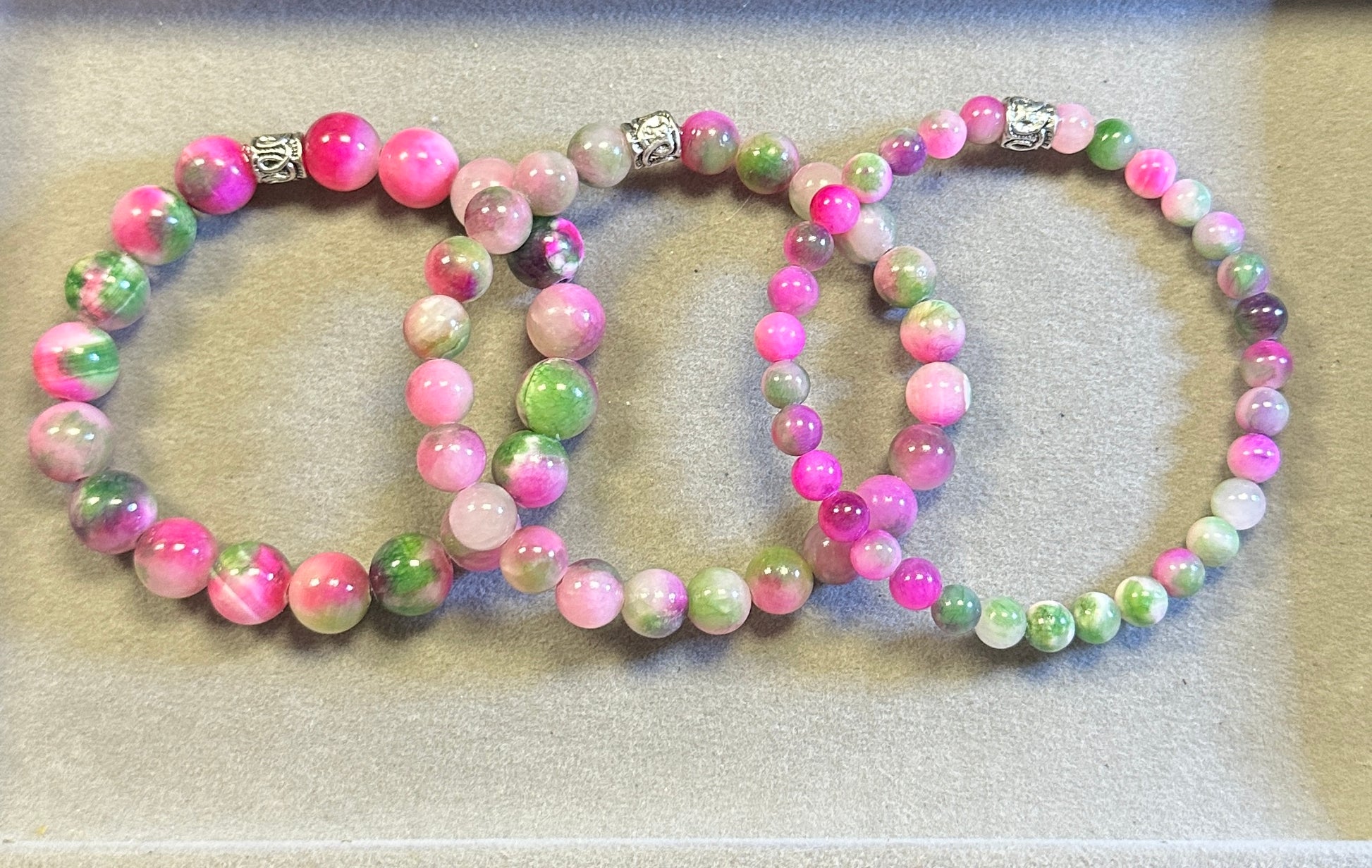 Two beaded bracelets with pink, green, and white beads on a light background