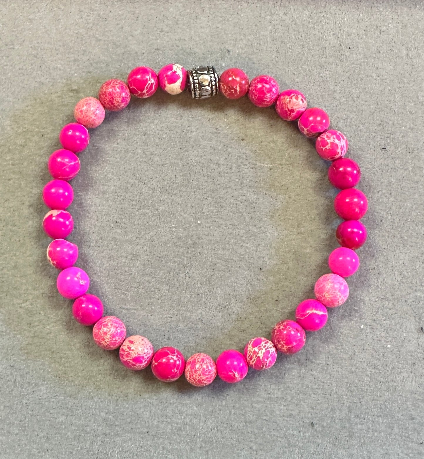 Pink beaded bracelet with a silver charm on a gray surface